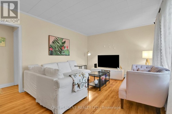 Living room with white sofas, a television, and hardwood floors. - 36 Argue Drive, Ottawa