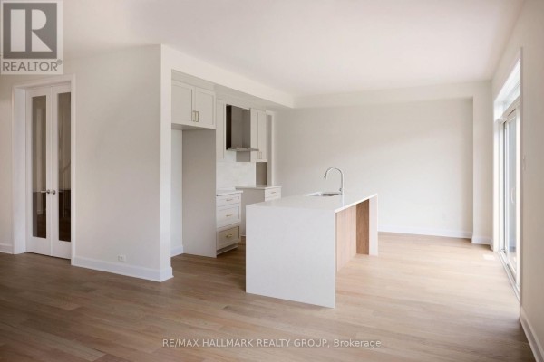 Open concept living area showing a white kitchen island and cabinetry with wood flooring. - 36 Big Dipper Street, Ottawa