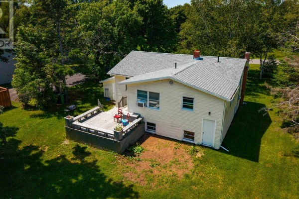 Rear exterior view of the yellow house with a wooden deck and green lawn. - 36 Bonavista Drive, Cornwall