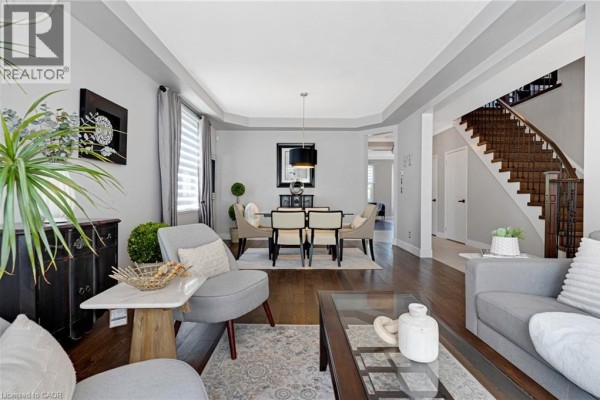 Living room and dining room with grey seating, dark wood floors, and a grand wooden staircase. - 36 Dellgrove Circle, Cambridge