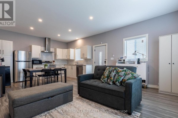 Open-concept living, dining, and kitchen area with grey walls and laminate flooring. - 36 Division Street, St  Catharines