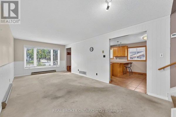Living room with a large window, beige carpet, and a view of the kitchen. - 36 Dutch Settlers Court, East Gwillimbury