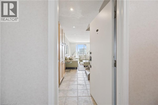 View from apartment doorway into living room with beige sofa and tiled entryway. - 36 Hayhurst Road Unit# 329, Brantford