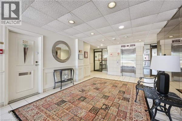 Hallway in apartment building with elevator, ornate rug, and decorative table. - 36 Hayhurst Road Unit# 329, Brantford