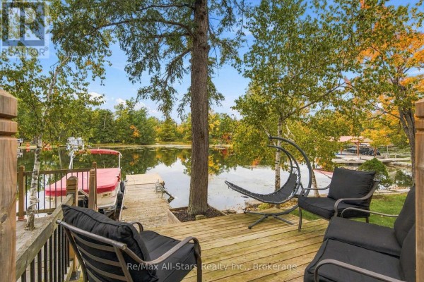 Wooden deck with black patio furniture overlooking a calm lake with a boat docked. - 36 Jack Pine Way, Trent Lakes