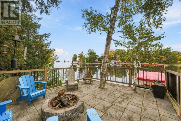 Stone patio with a fire pit and blue Adirondack chairs facing the lake. - 36 Jack Pine Way, Trent Lakes