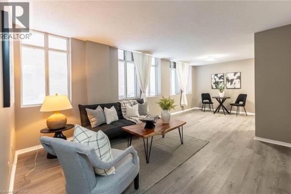 Living room with a sofa, chairs, coffee table, and large windows with white curtains. - 36 James Street S Unit# 303, Hamilton