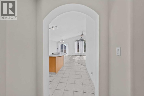 View through an arched doorway into a bright living room with a vaulted ceiling and large windows. - 36 Kodiak Boulevard N, Lethbridge