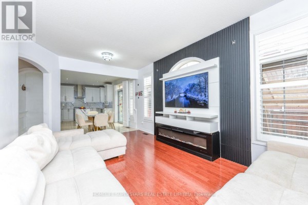 Living room with a sectional sofa, entertainment unit, fireplace, and an adjacent dining area. - 36 Lucky Lane, Brampton