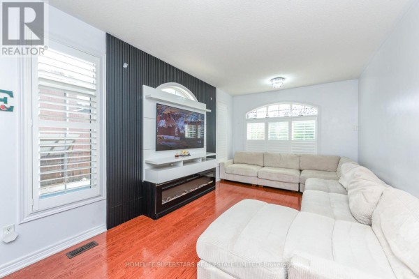 Living room with a sectional sofa, dark wood accent wall, entertainment unit, and light-colored sofa. - 36 Lucky Lane, Brampton