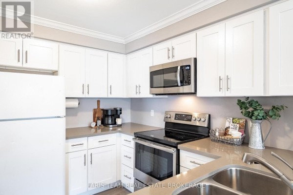 Kitchen with white cabinets, stainless steel appliances, and grey countertops, showing the stove and sink area. - 36 Red Oak Drive, Barrie