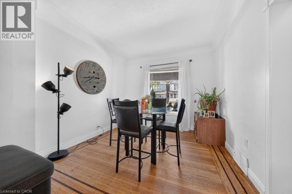 Dining area with a glass-top table, black chairs, and a window overlooking the street. - 36 Sherman Avenue N, Hamilton