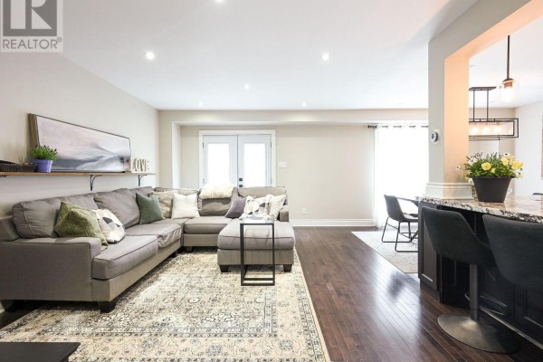 Living room with a large grey sectional sofa, patterned rug, and dark hardwood floors. - 36 Sprucedale Court, Brampton