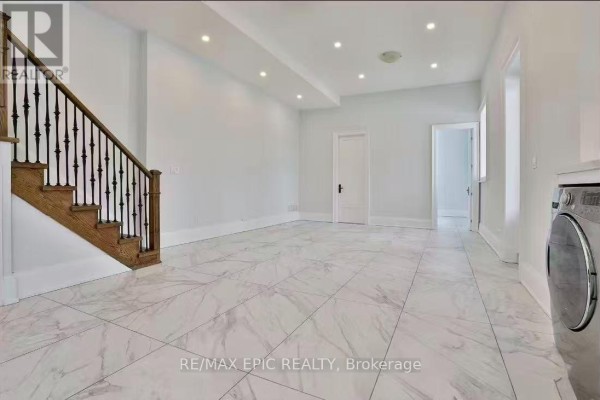 Spacious living area with white walls, white tiled floor, and a wooden staircase. - 36 Sussex Avenue, Richmond Hill