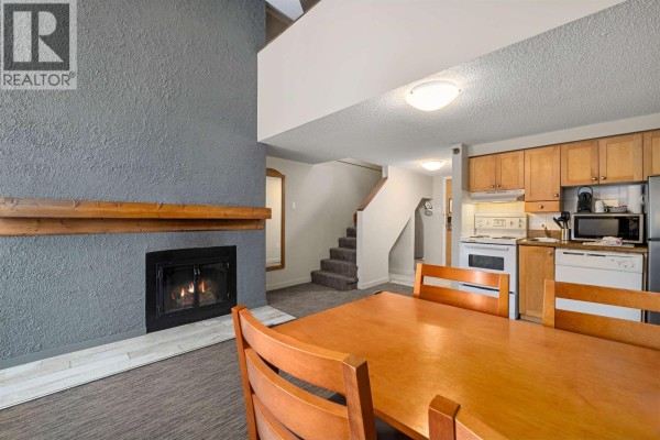 View of the fireplace, dining area with wooden table, and kitchen with white appliances. - 360 4429 Sundial Place, Whistler