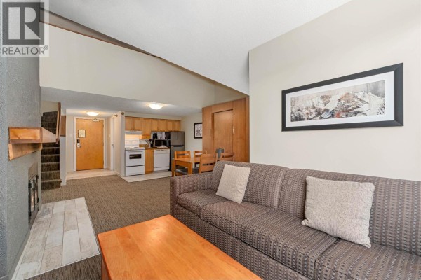 Living room sofa with mountain artwork above, view of the kitchen, and a stairway. - 360 4429 Sundial Place, Whistler