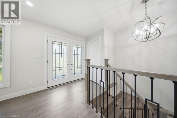 Interior entryway with light wood floors, modern light fixture, and a staircase with black railings. - 360 Bishopsgate Road, Burford