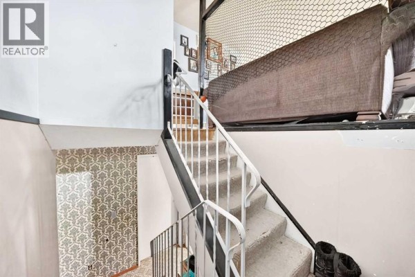 Carpeted stairs with white railings lead up to a landing with patterned wallpaper. - 360 Rundlefield Road Ne, Calgary