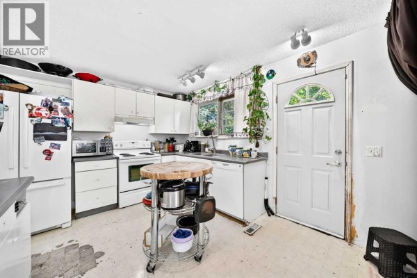 White kitchen with white cabinets, appliances, and a door leading outside. - 360 Rundlefield Road Ne, Calgary
