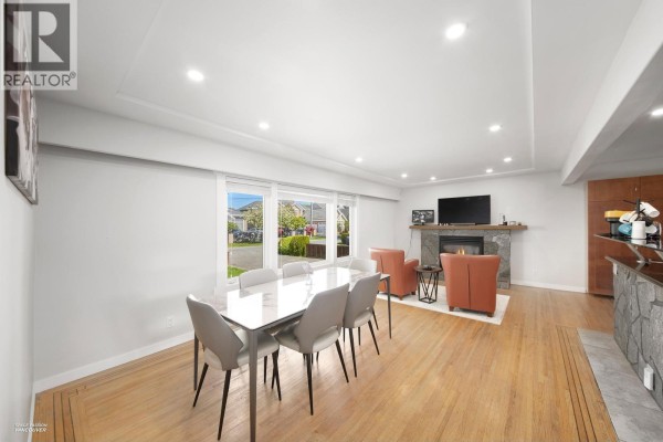 Dining area with a white table, grey chairs, and a stone fireplace in the living room. - 3600 Raymond Avenue, Richmond