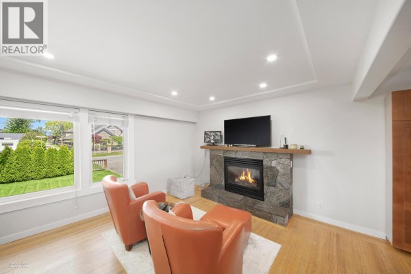 Living room area with two orange chairs, ottoman, and a stone-clad fireplace with a television. - 3600 Raymond Avenue, Richmond
