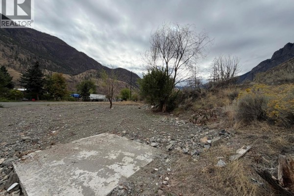Undeveloped lot with a concrete slab, gravel, rocks, and sparse vegetation against a backdrop of hills. - 3601 Big Horn Curl, Ashcroft