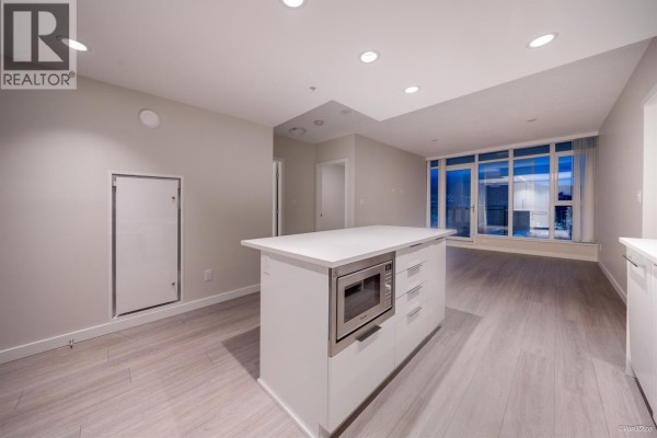 Open concept kitchen with white island, integrated microwave, and light wood flooring. - 3602 1182 Westwood Street, Coquitlam