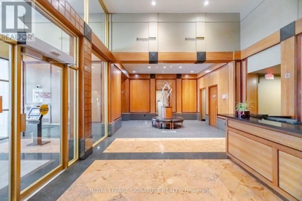 Interior lobby with wood paneling, marble floors, a sculpture, and elevator access. - 3603 - 750 Bay Street, Toronto