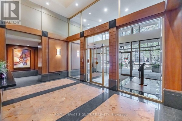 Apartment building lobby with wood accents, marble flooring, and glass entrances. - 3603 - 750 Bay Street, Toronto