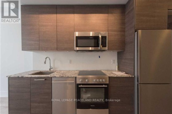 Kitchenette with dark wood cabinets, stainless steel appliances, and granite countertops. - 3604 - 28 Wellesley Street E, Toronto