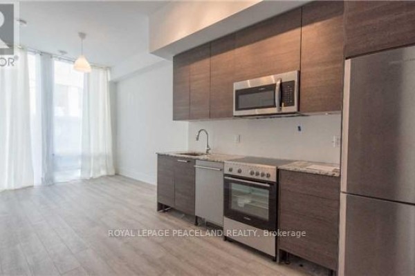 Kitchenette with dark wood cabinets, stainless steel appliances, and granite countertops, opening to living area. - 3604 - 28 Wellesley Street E, Toronto