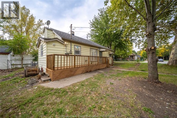 Rear exterior of a beige bungalow showing a wooden deck and grassy yard. - 3605 Bloomfield, Windsor