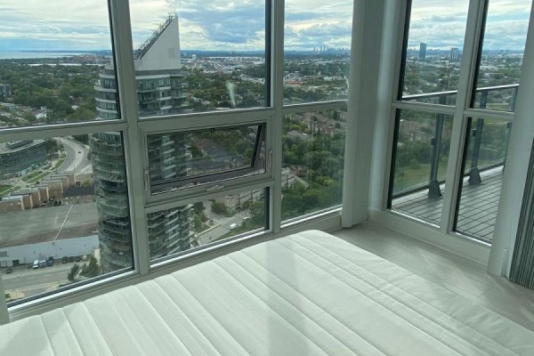 Bedroom with large windows offering a panoramic view of the city and surrounding landscape. - 3606 - 2212 Lakeshore Road W, Toronto