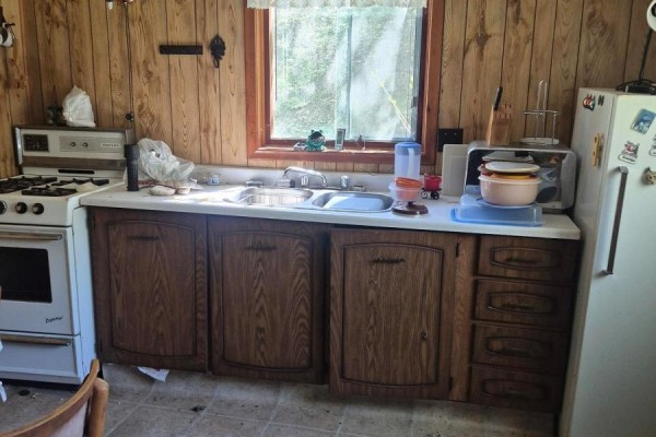 Kitchen area with wood-paneled walls, a white stove, double sink, white countertop, and wooden cabinets. - 3606 County Road 620, North Kawartha