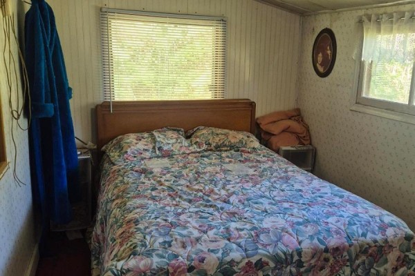 Bedroom with a floral comforter on the bed, a wooden headboard, and patterned wallpaper. - 3606 County Road 620, North Kawartha