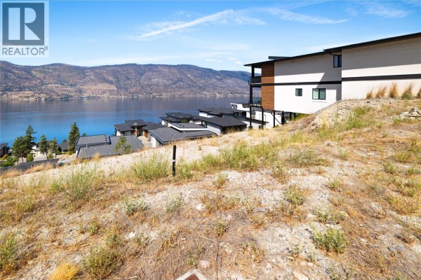 Slope with dry vegetation overlooks modern homes and Okanagan Lake under a blue sky. - 3608 Sagehill Court, Kelowna