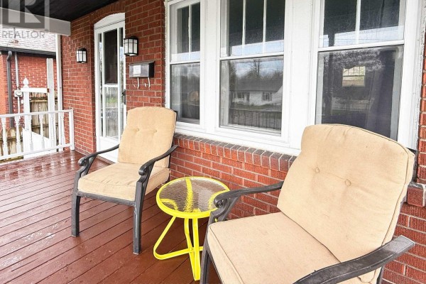 Two tan upholstered chairs and a small yellow table on the wooden front porch. - 361 Bowen Road, Fort Erie