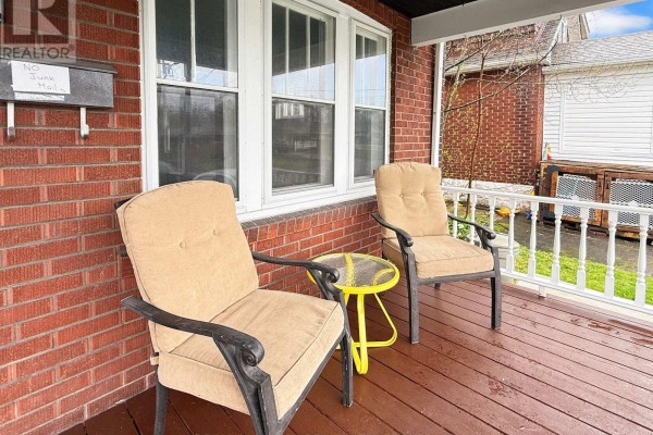 Close-up of the wooden front porch with two chairs, a yellow table, and a brick wall. - 361 Bowen Road, Fort Erie