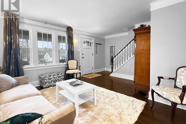 Living room with a beige sofa, white coffee table, rug, antique armoire, and staircase. - 361 Bowen Road, Fort Erie