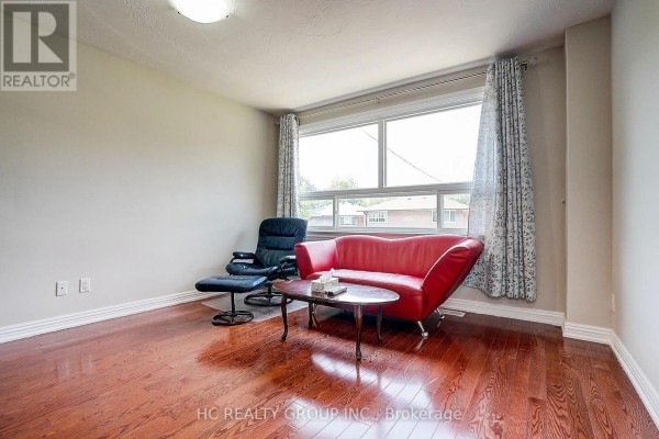 Living room with a red sofa, black recliner, coffee table, and hardwood floors. - 361 Highfield Road, Toronto