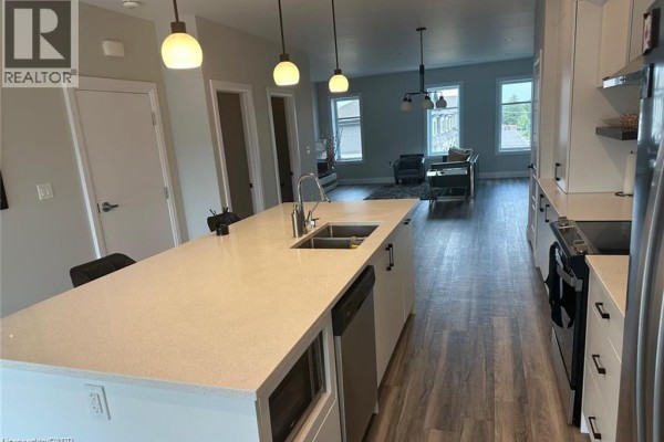 Open concept living area with a kitchen island, stainless steel appliances, and living room view. - 361 Quarter Town Line Unit# 108, Tillsonburg