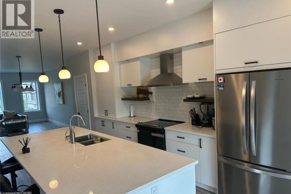 Kitchen with white cabinets, stainless steel appliances, subway tile backsplash, and a large island. - 361 Quarter Town Line Unit# 108, Tillsonburg