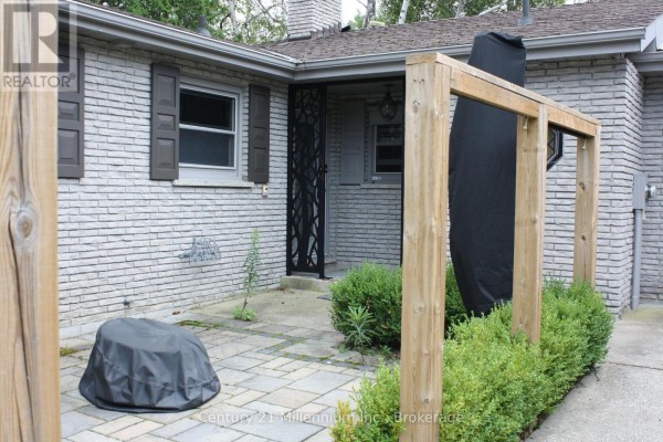 Close-up of the front entrance with a stone patio, wooden pergola, and decorative metal screen door. - 361 Tyendinaga Drive N, Saugeen Shores