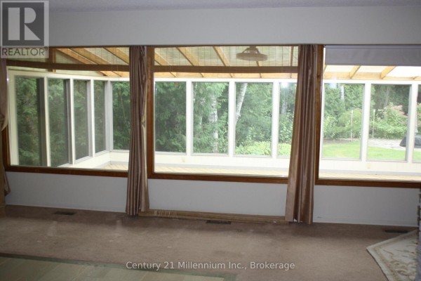 Sunroom with large windows overlooking a wooded backyard, featuring beige carpet and curtains. - 361 Tyendinaga Drive N, Saugeen Shores