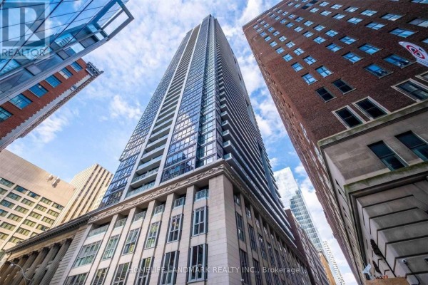 Exterior view looking up at a tall glass and concrete apartment building with brick accents. - 3610 - 70 Temperance Street, Toronto