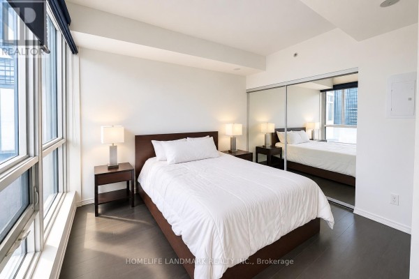 Master bedroom with a queen bed, nightstands, and a mirrored closet reflecting the city view. - 3610 - 70 Temperance Street, Toronto