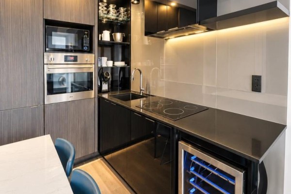 Modern kitchen with stainless steel appliances, wine fridge, black countertops, and dark wood cabinetry. - 3610 - 70 Temperance Street, Toronto
