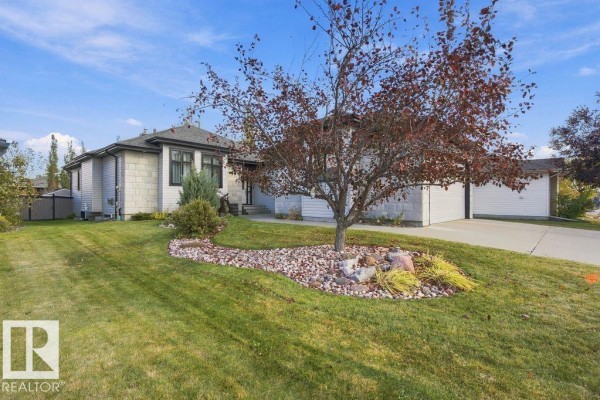 Front exterior of the house with a green lawn and mature tree. - 3611 61 St, Beaumont