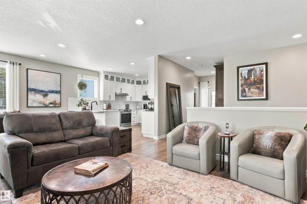 Living room with a dark sofa, two chairs, and a kitchen view. - 3611 61 St, Beaumont