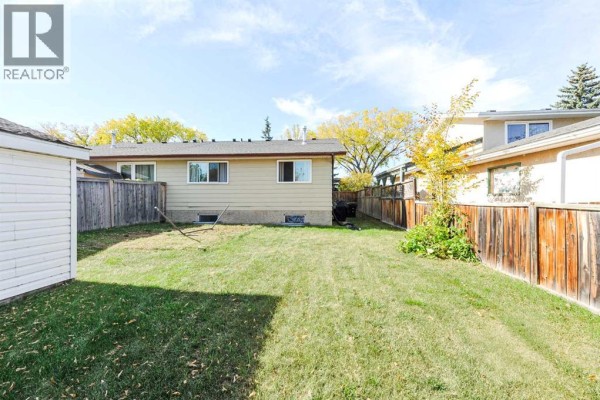 View across the backyard showing the rear of the duplex, surrounded by wooden fences and neighboring houses under a blue sky. - 3611b 66a Street, Camrose